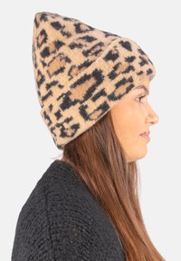 Knit beanie in tan and black leopard print, featuring a pointed crown and soft texture. Worn at an angle on a model.