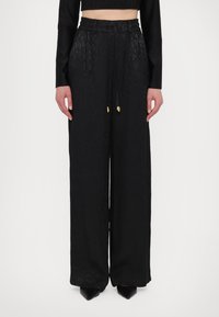 Zwarte wijde broek met subtiele dierenprint, elastische tailleband met trekkoord en accenten van goudkleurig beslag.