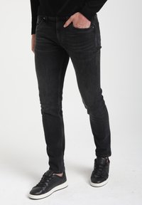 Sleek mustad denim püksid kerge pleekimisega, rõhutatult tikitud detailidega ja viie taskuga disain, koos mustade tennistega valgete tallaga.