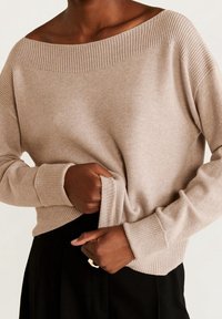 Beige gestrickter Pullover mit weitem Bootsausschnitt, gerippten Bündchen und Saum, der eine weiche Textur und einen entspannten Schnitt aufweist.