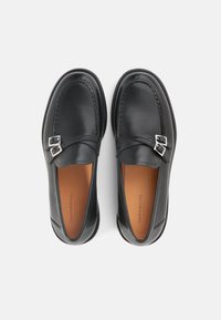 Μαύρα δερμάτινα μοκασίνια με κομψό σχεδιασμό, διαθέτουν ασημένιες αγκράφες και λεία υφή. Καφέ εσωτερική σόλα με εμφανές λογότυπο.