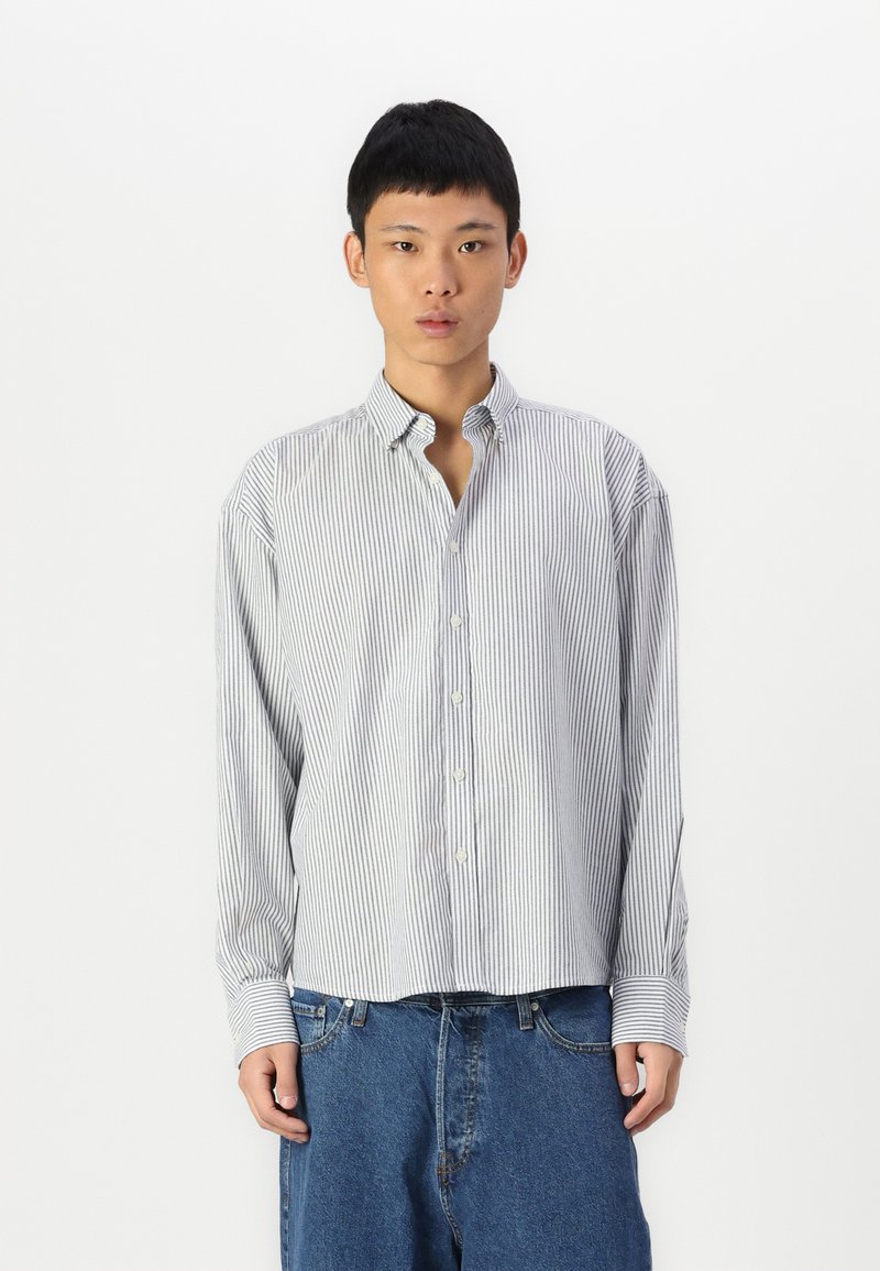 Chemise à manches longues à rayures blanches et bleu marine ; comprend un col, une coupe décontractée et des poignets en tissu légèrement texturé.