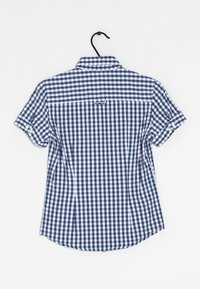 Camisa de cuadros de manga corta en algodón azul y blanco. Cuenta con un cuello abotonado, yugo trasero y mangas enrolladas con acentos de botón.