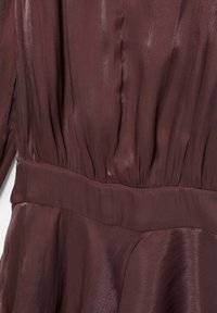 Obleka bordo barve z gladko, teksturirano površino, ki ima oprijet pas, naborke, ki se raztezajo od živca, in dolge rokave.