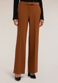 Bruine wijde broek van gladde stof, met een ceintuur in de taille en een gouden gesp, scherpe plooien en gecombineerd met zwarte hakken.