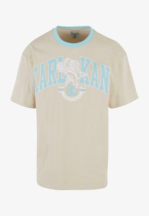 Camiseta de algodón beige con cuello redondo acanalado azul y corte oversized, que presenta un gran gráfico en blanco y azul con el diseño de un pájaro que dice "KARL KANI".