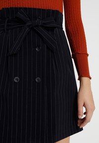 Marinblå rutigt kjol med midjeband, med dubbel knappar och en strukturerad form, presenterad med en ribbad röd tröja.