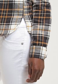 Camisa de cuadros con colores negro, blanco y mostaza; confeccionada en tela suave; diseño ajustado con mangas con puños y aberturas laterales.