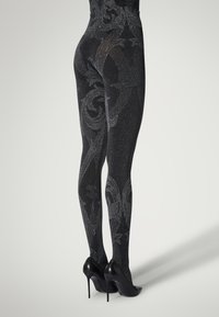 Collant neri con un motivo scintillante, caratterizzato da eleganti spirali e forme. Indossati con scarpe con tacco alto nere, che mettono in risalto texture e brillantezza.