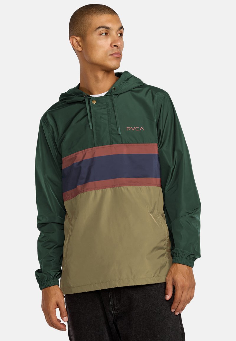 Anorak leggero con cappuccio di colore verde scuro, con strisce bordeaux e blu navy attraversa il petto. Presenta polsini elasticizzati e cappuccio regolabile.