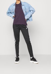 Ljusblå denimjacka över en lila t-shirt, ihop med svarta smala byxor med vita sidostråk och svarta sportskor.