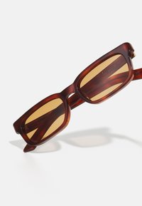 Gafas de sol rectangulares con tinte marrón, con un marco de plástico brillante y lentes amarillos, que presentan patillas delgadas y un diseño retro.