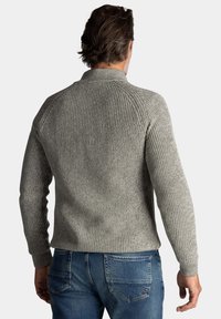 Grijze ribgebreide trui met hoge kraag en raglanmouwen, gecombineerd met blauwe denim spijkerbroek, met een gestructureerde stof.
