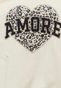 Tela cremoso con un estampado de corazón de leopardo negro y dorado. El texto centrado dice "AMORE" en letras negritas y negras con un acabado brillante.