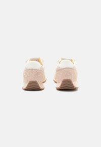 Sneakers with a textured light pink suede upper, white leather accents, and a beige rubber sole featuring a wavy tread pattern.