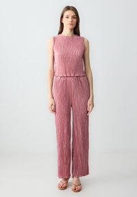 Jumpsuit senza maniche color rosa con texture plissettata, vita elastica e pantaloni a gamba larga, realizzato in tessuto leggero.