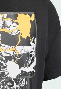 Czarny t-shirt z odważnym nadrukiem graficznym łączącym białe i żółte elementy, przedstawiający dynamiczne ilustracje i szczegóły w stylu komiksowym.