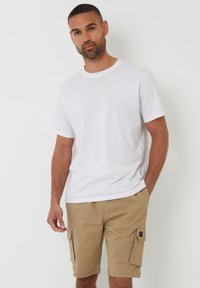 Hvid t-shirt med korte ærmer kombineret med khaki cargo shorts med sidelommer og et lille logo på den venstre lomme.