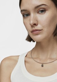 Collar de metal con un acabado plateado suave y un pequeño colgante con acentos dorados que se asemeja a una flor o a una forma abstracta.
