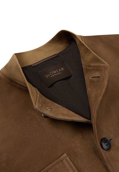 Bruine suède jas met geribbelde kraag, knoopsluiting en een binnenlabel met de tekst "Slowear Montedoro" op een zwarte stoffen voering.