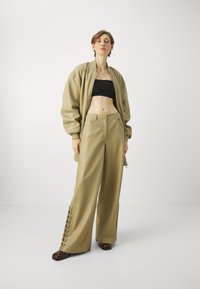 Béžová bombera, čierny crop top a široké nohavice s šnurovaním a kovovými očkami. Hladká textura, uvoľnený strih.