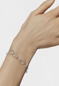 Pulsera de cadena de plata con eslabones interconectados en forma de flor. Textura suave con un acabado pulido, llevada en una muñeca.