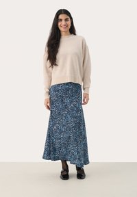 Pull en maille beige avec un col rond associé à une longue jupe bleue à motif floral. Des chaussures noires complètent l'ensemble.