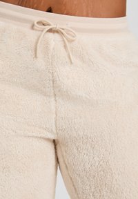Fleece loungewear broek in zacht beige met een geribde tailleband en verstelbaar trekkoord. Heeft een fluffige textuur en een comfortabele pasvorm.