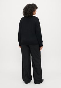 Pulover negru supradimensionat din tricot, asortat cu pantaloni negri largi. Textură netedă, design minimalist și o siluetă relaxată.