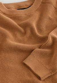 Pull en laine marron avec un motif en côtes texturé, un col rond et un détail de poignet replié, en tissu doux qui drape.