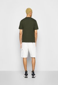 T-shirt en coton vert olive, associée à un short cargo blanc. Baskets montantes noires avec logo étoile et semelle blanche. Design simple et décontracté.