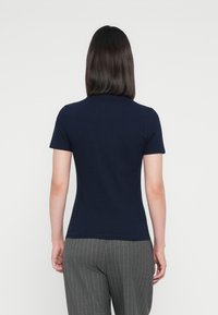 Camiseta ajustada de color azul marino con mangas cortas y escote redondo, combinada con pantalones grises de rayas que destacan por su textura suave y lisa.