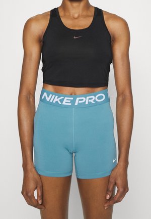 Person trägt schwarzen Nike Crop Tank Top und blaue Nike Pro Kompressionsshorts vor einfachem Hintergrund.