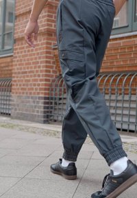 Pantaloni cargo grigi realizzati in un materiale leggero e resistente all'acqua, con polsini elastici, tasche laterali e una discreta etichetta con logo sulla coscia.