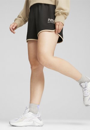 Zwarte sportshorts met een gestructureerde stof, beige afwerking en een wit "Puma" logo. Geverfd met witte sneakers en grijze enkel sokken.