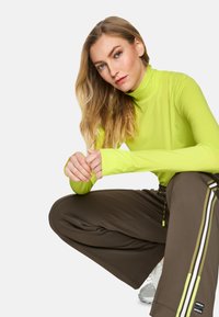 Bright yellow long-sleeve top with high collar, paired with dark brown loose-fit pants featuring side stripes and textured fabric.