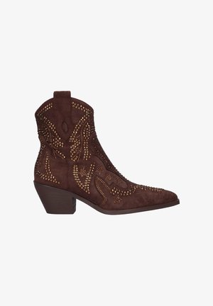 Botín de ante marrón con punta afilada, adornado con tachuelas doradas, que presenta costuras de estilo western y un tacón corto apilado.