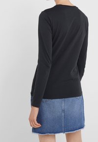 Musta pitkähihaispaita pyöreällä pääntiellä, yhdistetty revityillä reunoilla olevaan farkkuhameeseen. Puuvillakangas, yksinkertainen muotoilu.