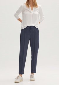 Vit långärmad blus med v-ringning, matchad med navy tapered byxor med dragsko i midjan och uppvikta ärmar, bärs med vita sneakers.