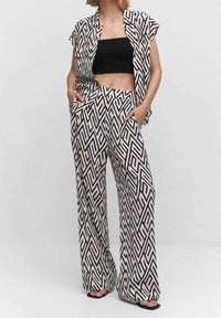 Ensemble en deux pièces à motif noir et blanc ; chemise à manches courtes avec un design géométrique, pantalon à coupe ample avec poches latérales.