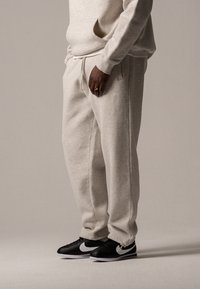 Hellgraue, weiche Fleece-Sweatpants mit elastischem Bund und Seitentaschen. Kombiniert mit schwarzen Sneakers mit weißen Swoosh-Details.