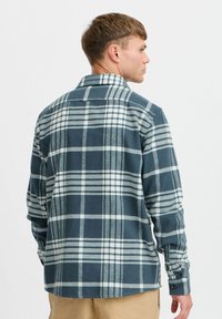 Flannel shirt in dark teal with white and gray plaid pattern. Long sleeves, button cuffs, and a classic collar. Soft, textured fabric.