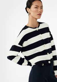 Cardigan a righe in navy e bianco, caratterizzato da scollatura rotonda, maniche lunghe e chiusura a bottoni davanti. Texture morbida.