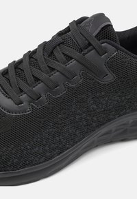 Black athletic shoe featuring mesh and synthetic upper, textured surface, lace-up design, and a flexible rubber sole with geometric patterns.