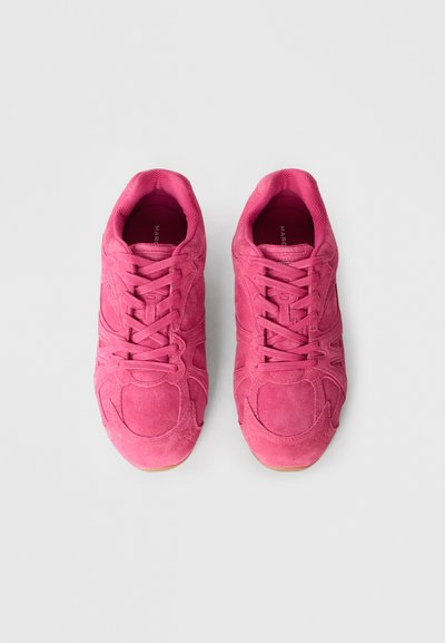 Różowe sportowe buty zamszowe z zaokrąglonym noskiem, wiązane sznurowadłami, teksturowaną powierzchnią i kontrastową, gumową podeszwą. Widok z góry ukazuje szczegó�ły buta.