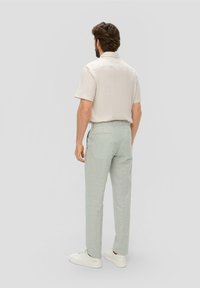 Chemise beige clair à manches courtes associée à un pantalon à carreaux vert menthe et des baskets blanches, vue de dos.
