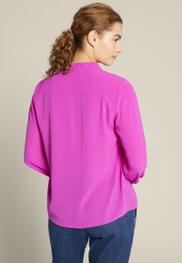 Fuchsia-Bluse mit langen Ärmeln, lockerer Passform und abgerundetem Saum. Der Rücken verfügt über eine Schulternaht für zusätzliche Struktur. Glatte Stofftextur.