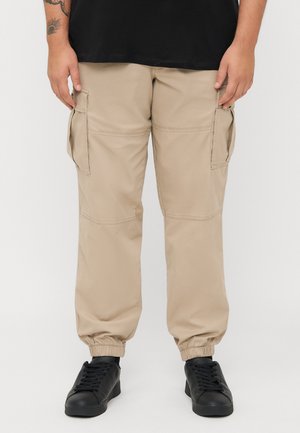 Beige cargo pants with elastic cuffs, side pockets, and a smooth texture. Worn with black sneakers, featuring a minimalist design.
