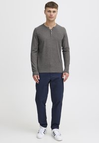 Cămașă henley cu mânecă lungă, de culoare gri închis, cu trei nasturi la gât, asociată cu pantaloni navy și adidași albi cu dungi negre.