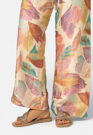 Pantalones anchos y ligeros con estampado de hojas multicolores, combinados con sandalias beige de punta abierta que tienen correas decorativas en forma de hojas.